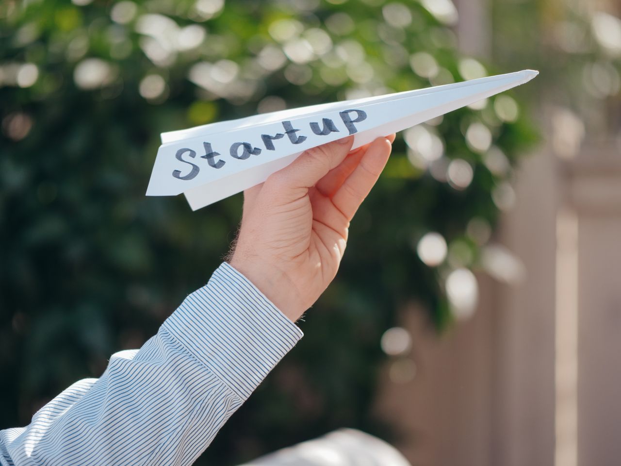 Close-up of a hand holding a paper plane with Startup written, symbolizing a business launch.